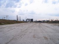 a dirt road in an empty city during the day time with clouds above it's tops