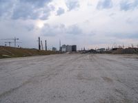 a dirt road in an empty city during the day time with clouds above it's tops