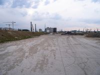 a dirt road in an empty city during the day time with clouds above it's tops