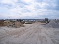 a train bridge and dirt is over a road near a body of water with sand