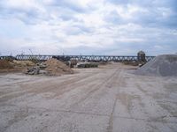 a train bridge and dirt is over a road near a body of water with sand