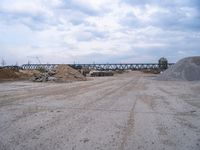 a train bridge and dirt is over a road near a body of water with sand