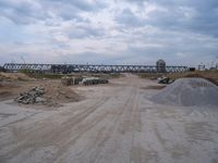 a train bridge and dirt is over a road near a body of water with sand