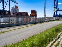 an empty road with containers on either side and cranes in the back ground behind it