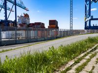 an empty road with containers on either side and cranes in the back ground behind it