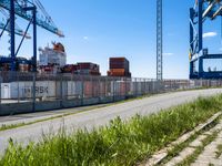 an empty road with containers on either side and cranes in the back ground behind it