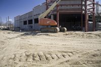 a large building under construction on top of sand in front of a building on the side of a road