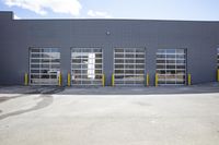 a large gray warehouse with large sliding doors and fire hydrants and a blue sky in the background