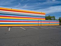 an empty parking lot painted brightly stripes on the wall of the building and sky as well as stones