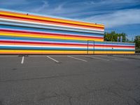 an empty parking lot painted brightly stripes on the wall of the building and sky as well as stones