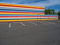 an empty parking lot painted brightly stripes on the wall of the building and sky as well as stones