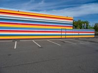 an empty parking lot painted brightly stripes on the wall of the building and sky as well as stones