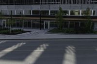 a tall building near an empty street with windows and trees in front of it and a white fire hydrant sitting on the corner