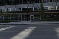 a tall building near an empty street with windows and trees in front of it and a white fire hydrant sitting on the corner