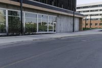 an empty city street in front of a business building with tall windows and a tree on the sidewalk