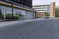 an empty city street in front of a business building with tall windows and a tree on the sidewalk