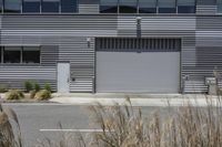 an industrial garage with doors closed to the street while tall grass line the driveway near it