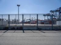 a concrete wall with a gated in area next to buildings and cranes in the background