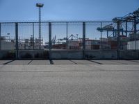 a concrete wall with a gated in area next to buildings and cranes in the background