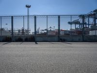 a concrete wall with a gated in area next to buildings and cranes in the background