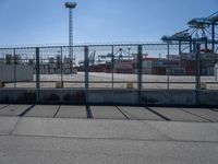 a concrete wall with a gated in area next to buildings and cranes in the background