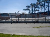 a concrete wall with a gated in area next to buildings and cranes in the background