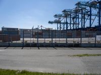 a concrete wall with a gated in area next to buildings and cranes in the background