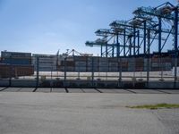 a concrete wall with a gated in area next to buildings and cranes in the background