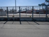 a concrete wall with a gated in area next to buildings and cranes in the background