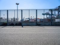 a large caged off area near two construction cranes and a lot of docks behind it