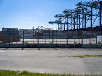 a large caged off area near two construction cranes and a lot of docks behind it