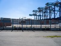 a large caged off area near two construction cranes and a lot of docks behind it