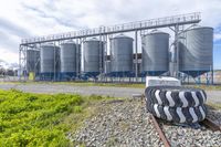 a set of four metal silos in front of two trains on the tracks with grass