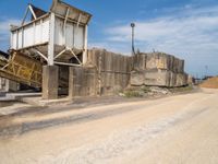 an old run down concrete building sits on the side of the road beside a dirt road