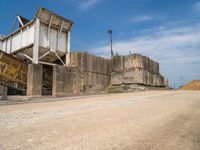 an old run down concrete building sits on the side of the road beside a dirt road