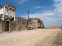 an old run down concrete building sits on the side of the road beside a dirt road