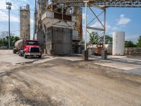 a large red truck parked at a factory with water running by it's side