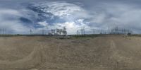 a small, empty dirt lot with multiple electrical towers on the hill side and blue cloudy sky