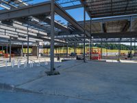 a large industrial steel building is under construction under blue sky with people walking by it