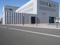 an empty street with a white building behind it's gray sideline on a clear day