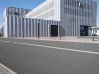 an empty street with a white building behind it's gray sideline on a clear day