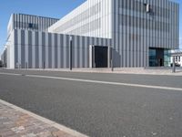 an empty street with a white building behind it's gray sideline on a clear day