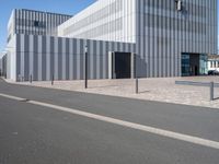 an empty street with a white building behind it's gray sideline on a clear day