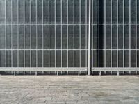 the sidewalk is lined with grey tile bricks and cement squares and a black wall behind