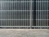 the sidewalk is lined with grey tile bricks and cement squares and a black wall behind