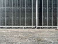 the sidewalk is lined with grey tile bricks and cement squares and a black wall behind