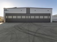 the industrial warehouse is painted gray and white and there are tires on the pavement to indicate where the space is going