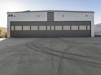 the industrial warehouse is painted gray and white and there are tires on the pavement to indicate where the space is going