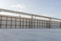 an empty lot with white concrete flooring and wall on the corner of it, under a metal structure