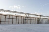 an empty lot with white concrete flooring and wall on the corner of it, under a metal structure